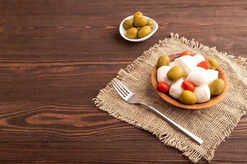 White Mozzarella cheese, with tomatoes and olives in wooden bowl on brown wooden background and