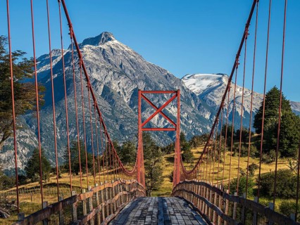 Old-style orange suspension bridge, river Rio Nadis south of Cochrane, mountain range at Rio Baker