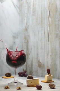 Glass of sparkling red wine next to cheese, grapes, nuts and figs, copy room