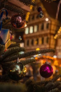 Shimmering Christmas baubles decorate the branches of a tree in front of festively illuminated