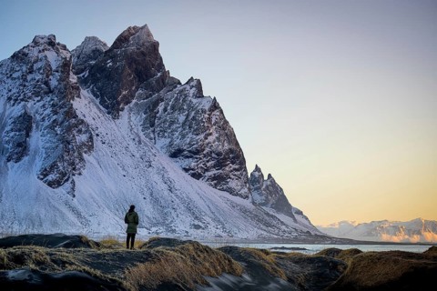 A lone traveler gazes at the majestic Stokksnes mountain in Iceland, covered in snow under a golden