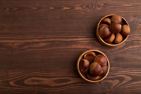 Wooden bowl with raw edible ?hestnuts on brown wooden background, top view, flat lay, copy space,