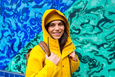 Young woman smiling in a vibrant yellow raincoat with backpack, exploring a san francisco street