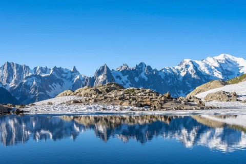 Young man in front of impressive mountain landscape in morning light, reflection in the Lac Blanc