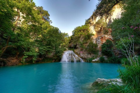 A waterfall flows into a large turquoise pool surrounded by green rocks and trees, waterfalls,
