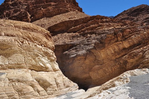 Brown rock formation with a narrow, dark entrance in a desert environment, Death Valley National
