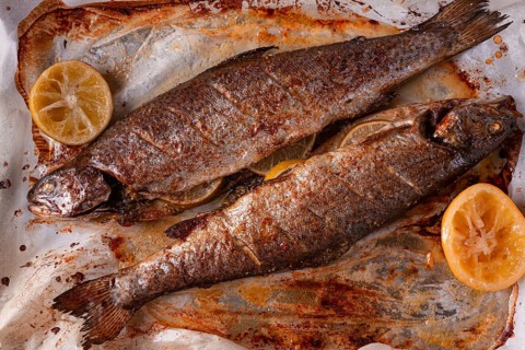 Two fish are being cooked on a baking sheet in a home kitchen. Lemon slices are placed beside the