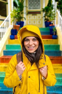 Happy young woman wearing a bright yellow raincoat and beanie smiling at the camera, standing in