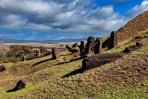 Lonely Moai statues stand leaning on a grassy hill under clouds, The Moai Statues on Easter Island