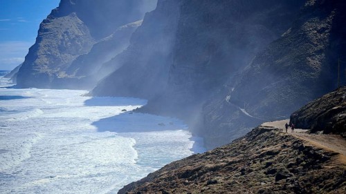 Dramatic coastline with steep cliffs and a misty path along the sea, spray, two hikers in the