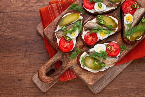 Sandwiches on rye bread with sprats, quail eggs, fresh tomatoes and pickled cucumber, on a wooden