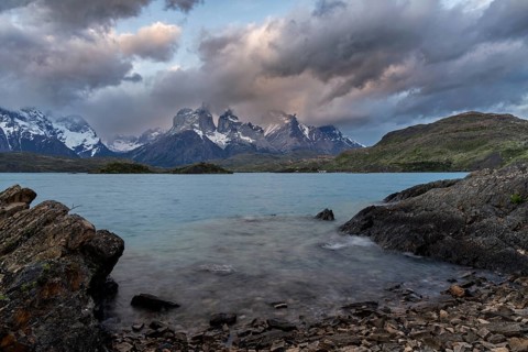 Cuernos del Paine with cloud atmosphere, turquoise Lake Pehoé with rocks in the foreground, Torres