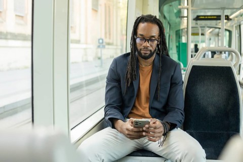 A cuban business man in a casual outfit uses his smartphone while seated on a modern, empty tram.