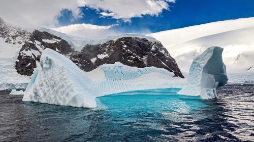 Frozen iceberg with arch-like structure details under a clear blue sky, icebergs in the landscape