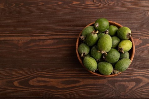 Ripe Feijoa in wooden bowl on brown wooden background, top view, flat lay, copy space, minimalism