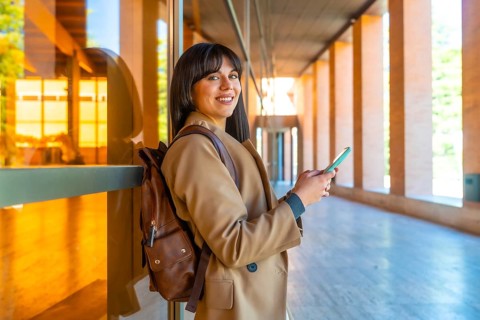 Young woman student wearing a brown backpack and coat, smiling and looking at the camera while
