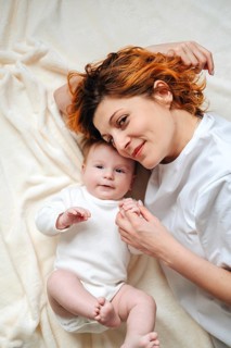 A mother and her newborn daughter share a loving moment lying on a soft blanket. The baby girl in
