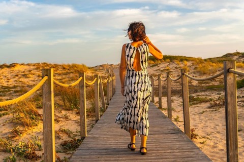 Woman walking along a wooden boardwalk through sand dunes towards the beach, enjoying the warm glow