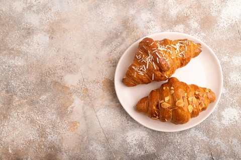 Croissant on white plate on brown concrete background, top view, flat lay, copy space