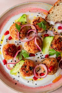 Close up of a vibrant dish featuring juicy meatballs on a bed of creamy yogurt. Garnished with