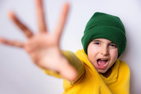 A lively child wearing a green beanie and yellow sweater extends their hand playfully towards the