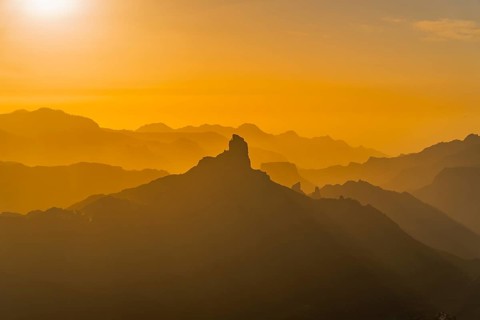 A captivating view of Roque Nublo under a golden sunset, showcasing layers of mountains bathed in