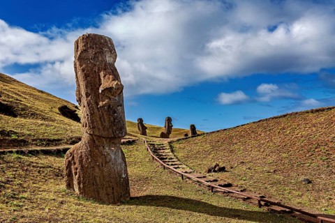 Several moais on a hill with a path surrounded by blue sky and clouds, The Moai statues on Easter