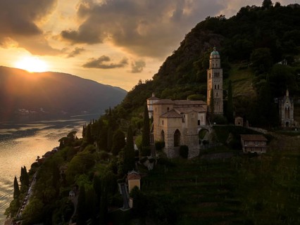 A stunning sunset view over Lake Lugano illuminates the historic architecture and lush landscape of