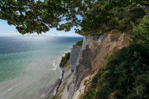 White chalk cliffs framed by green beech trees (Fagus sylvatica) with ships on the milky Baltic Sea