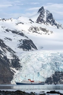 Expedition ship Ushuaia anchors in front of glacier front, snow-capped mountain peaks in the