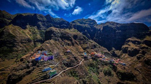 Panoramic view, small settlement, colorful village, nestled in raw, dramatic mountains under blue