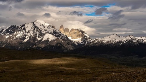 Torres del Paine granite peaks, snow-capped mountain peaks behind clouds, steppe landscape in the