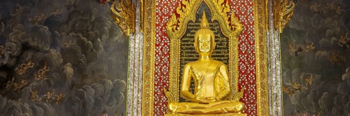 Golden meditating Buddha surrounded by wall paintings with Buddhist teachings and representations