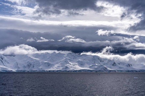 Snowy mountain coast with glacier edge at sea edge under dramatically cloudy sky, Antarctic
