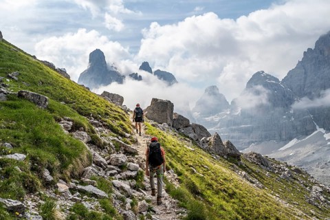 Two mountaineers on a hiking trail in front of a picturesque mountain landscape with rocky peaks,