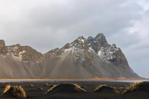 Sand dunes covered with rotten grass, lava sandy beach against mountain backdrop, winter,