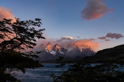 Cuernos del Paine at sunrise with pink clouds, Lake Pehoé in the foreground, framed by southern