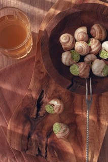 Snails cooked with herb oil on a wooden plate, served with white wine, natural light, no people