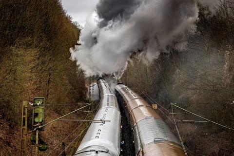 Black steam locomotive moves through wooded mystical route with powerful smoke, historic steam