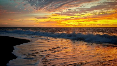 Impressive sunset with orange-golden sky over the sea and waves on the beach, hiking, Tarrafal de