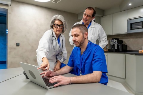Medical professionals in scrubs and lab coats collaborating on a laptop, sharing information, and