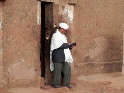 A man in traditional clothing is reading a book next to an old stone wall, UNESCO World Heritage