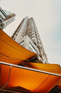 From below high-rise building framed by vibrant yellow awnings on a cloudy day in Hong Kong,