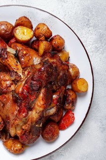 Pork knuckle baked with vegetables, new potatoes, on a white plate, homemade, no people