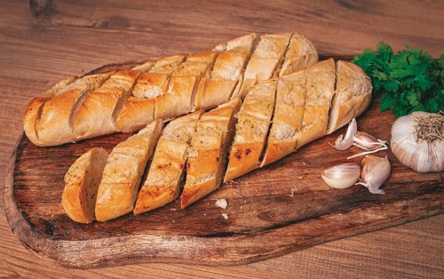 Garlic bread, baguette with garlic butter and herbs, on a wooden board, with herbs and garlic