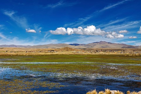 Open landscape with a water area in the foreground, surrounded by hills and a blue sky, The