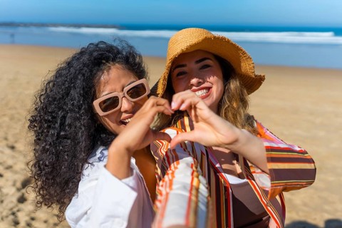 Two smiling young women celebrating their friendship and loving summer while doing a heart symbol
