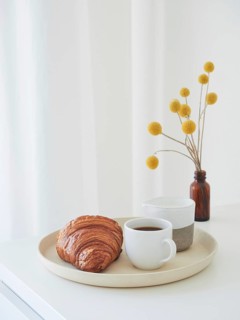 Minimalist lifestyle composition for breakfast. Tray with coffee cup, milk jug, croissant and amber