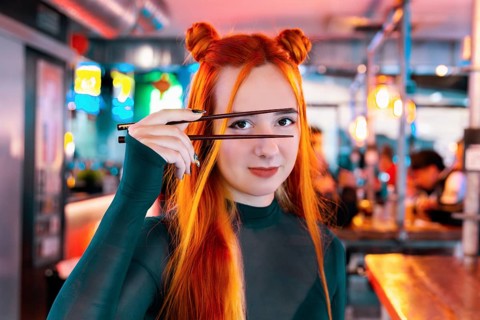 A young woman with vibrant hair and a stylish outfit enjoys her time at an Asian food market,