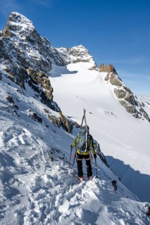 Mountaineer with skis at the fork Porta d'Es-cha, view of mountain peak Piz Kesch and glacier